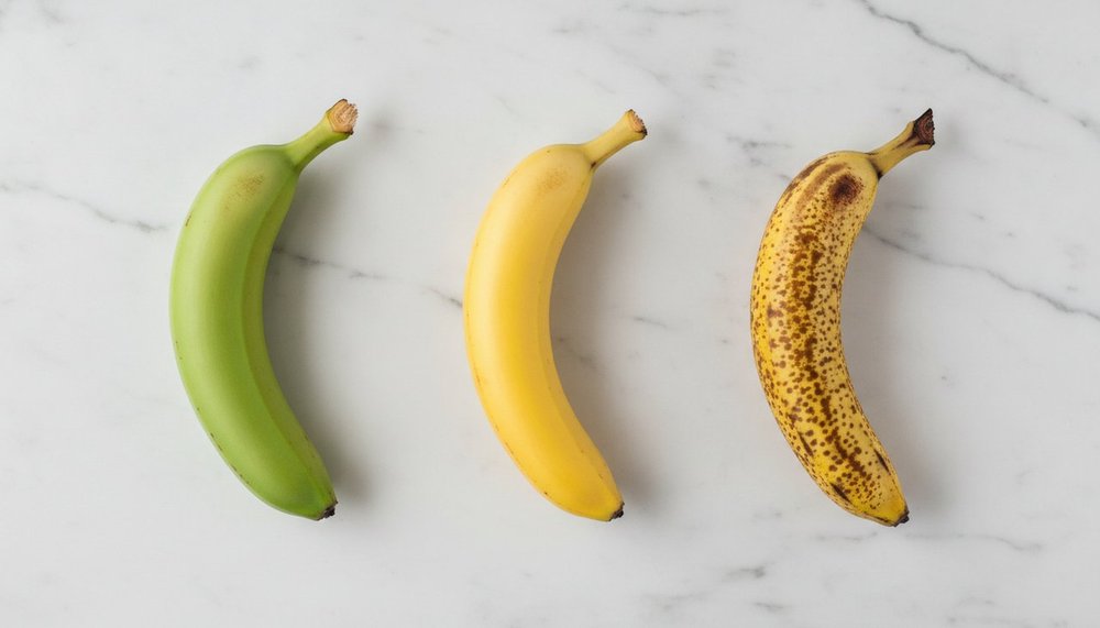 Trois bananes a des stades de maturite differents : verte, jaune et tachetee