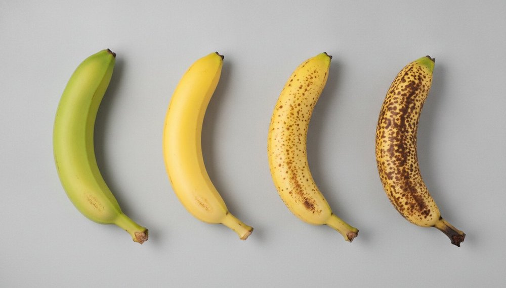 Quatre bananes alignées montrant quatre stades de maturité, de la banane verte à la banane tachetée